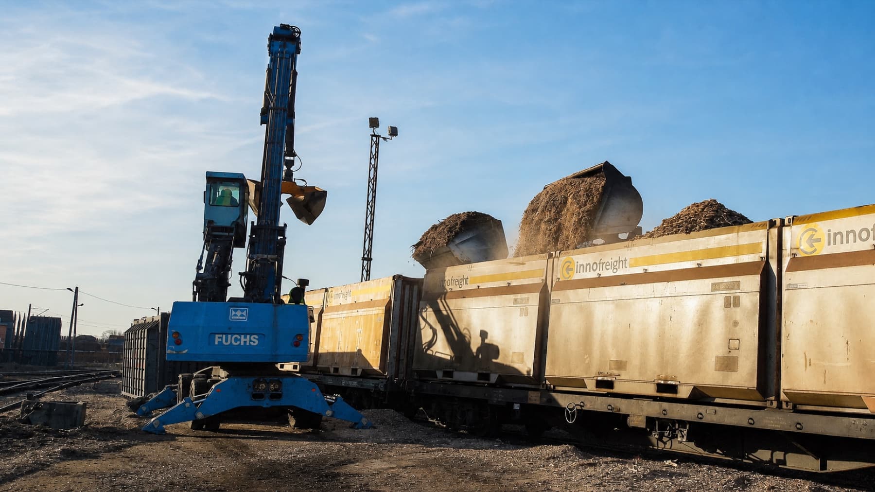 Załadunek biomasy drzewnej przeładowarką Fuchs do kontenerów Innofreight na wagonach kolejowych